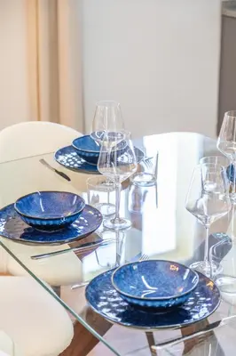 a glass table with blue plates and wine glasses at Résidence Casaviva in Calvi