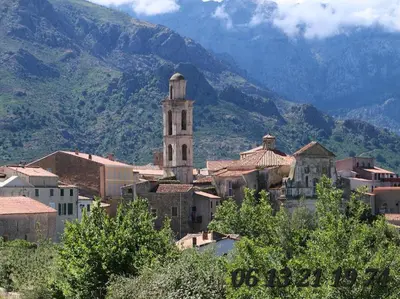 a town with a clock tower and mountains in the background at Appartement départ GR20 in Calenzana
