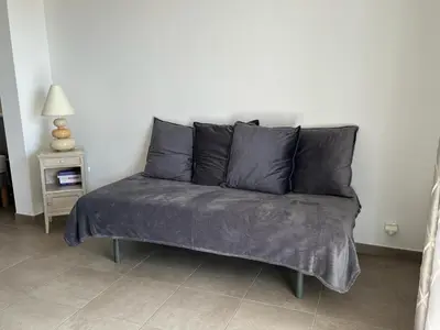 a couch with gray pillows in a living room at Studio 1 avec piscine & vue sur la baie d'Ajaccio in Alata