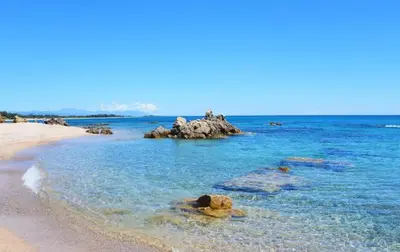 a beach with a group of people on a rock in the water at Palmeraie102 in Sari Solenzara