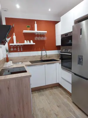 a kitchen with white cabinets and an orange wall at Palmeraie102 in Sari Solenzara