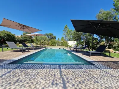 a swimming pool with two umbrellas and chairs at Villa ALVALMAX in Porto-Vecchio