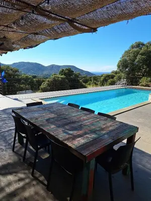 a wooden table and chairs next to a swimming pool at San Quilico - Maison climatisée piscine vue mer in Aregno
