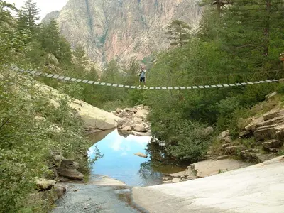 a person standing on a suspension bridge over a river at Résidence 3 étoiles Pietra Gemina - Appartements de vacances, au calme, avec Piscine in Calenzana