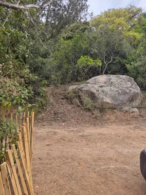 a fence next to a large rock and trees at Chalet maisonette dans hameau calme in Bonifacio