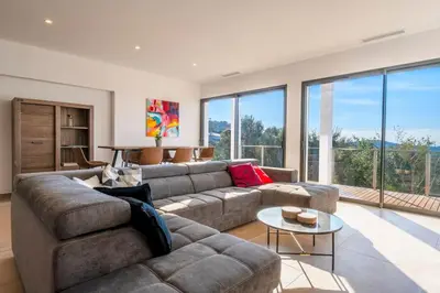 a living room with a large couch and large windows at Villa La Rondina vue mer, piscine et plage à pied. in Zonza