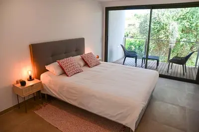 a bedroom with a bed and a balcony with chairs at Villa La Rondina vue mer, piscine et plage à pied. in Zonza