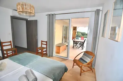 a bedroom with a bed and chairs and a balcony at Appartement 60m2 avec piscine privée dans villa in Oletta