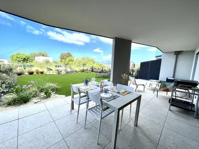 a patio with a table and chairs and a lawn at Appartement jardin de livia 2 rez de jardin in Porticcio