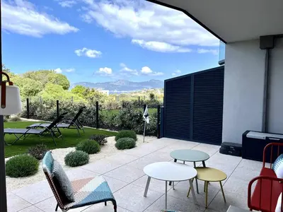 a patio with tables and chairs and a view of the mountains at Appartement jardin de livia 2 rez de jardin in Porticcio