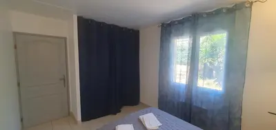 a bedroom with a bed and a window with blue curtains at Mini villa - T2 climatisé, proche des plages in Eccica-Suarella