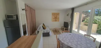 a living room with a table and a kitchen with a refrigerator at Mini villa - T2 climatisé, proche des plages in Eccica-Suarella