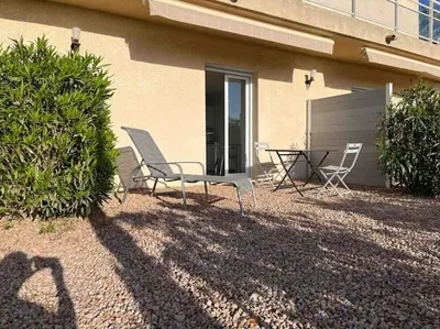 a patio with two chairs and a table in front of a building at Studio 2 avec piscine & vue sur la baie d'Ajaccio in Alata