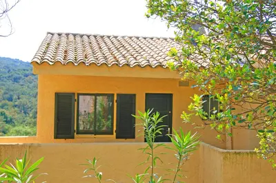 a house with black shuttered windows and a fence at Appartement charmant avec piscine à Porticcio - 32 m² in Porticcio