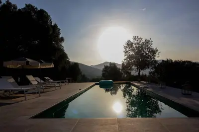 a swimming pool with chairs and the sun in the sky at VILLA A MUREDDA, piscine chauffée et vue mer in Olmeto