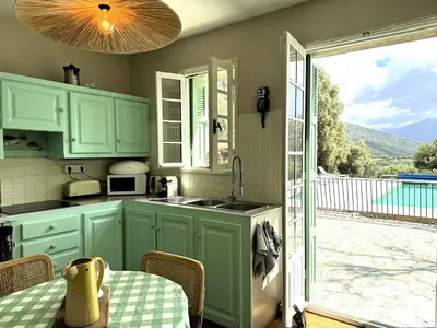 a kitchen with green cabinets and a table and a patio at VILLA A MUREDDA, piscine chauffée et vue mer in Olmeto