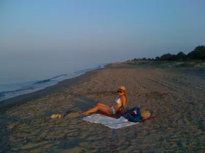 a woman sitting on a towel on the beach at Maison T2 500m de la plage in Poggio-Mezzana