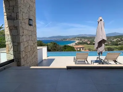 a patio with two chairs and an umbrella and a pool at VILLA RIVOLI vue mer et piscine in Pietrosella