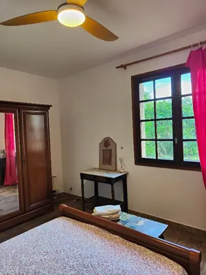 a bedroom with a bed with a ceiling fan and a table at Maison de campagne piscine et jardin privatifs près de la plage in Aléria