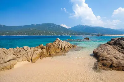 a beach with rocks and blue water and mountains at Appartement avec terrasse 3 pièces - Vue mer - Plage 5 min à pied in Propriano