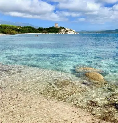 a beach with blue water and a castle in the background at Maison proche de la mer in Pianottoli-Caldarello
