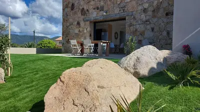 a stone house with two large rocks in a yard at Maison proche de la mer in Pianottoli-Caldarello