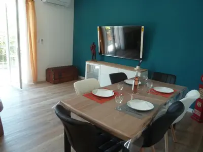 a dining room table with chairs and a television on the wall at Soleil & mer sur la Costa Verde in Cervione