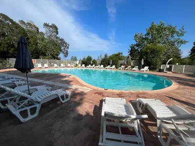 a swimming pool with lounge chairs and an umbrella at Mini Villa 63 proche plage dans résidence avec piscine à Favone in Sari Solenzara