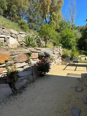 a stone retaining wall with flowers and plants at Maison de vacances in Aléria