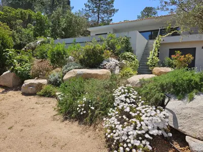 a garden with flowers and rocks in front of a house at Villa privée-piscine-vue mer-pinarello-cirindinu in Zonza