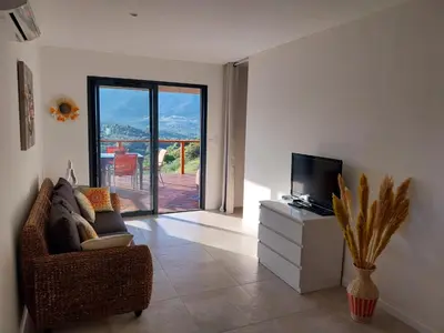 a living room with a couch and a tv on a dresser at Magnifique appartement entre mer et montagne in Tiuccia