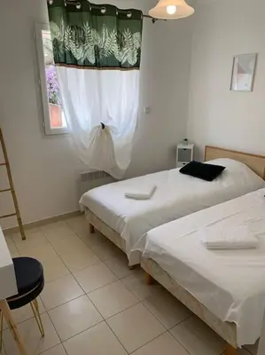 a bedroom with two beds and a window and a chair at Les Cistes Appt type 3 avec terrasse vue sur mer in Propriano