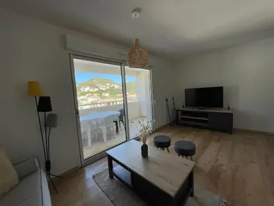 a living room with a table and a large window at T2 neuf port de Bonifacio avec parking privé in Bonifacio