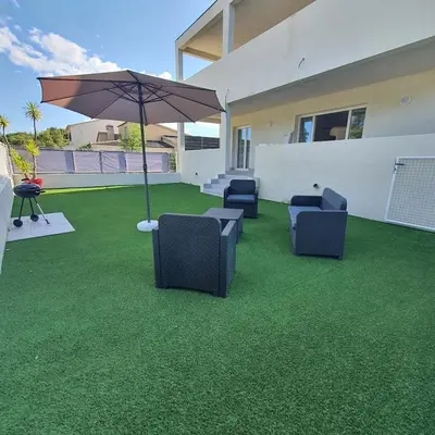 a patio with chairs and an umbrella on the grass at appartement Oliviaaxelle in Venzolasca