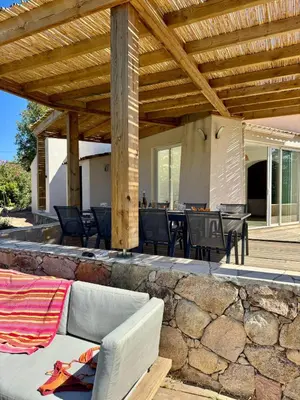 a patio with a stone wall and a wooden pergola at Villa avec Piscine proche plages et commerces in San-Gavino-di-Carbini
