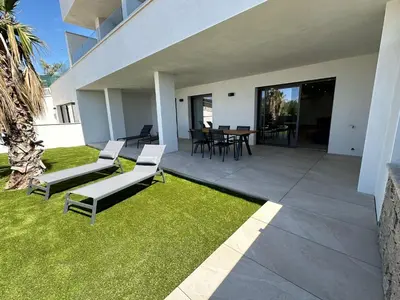 a patio with white chairs and a table and grass at Résidence du Château d'eau in Porticcio