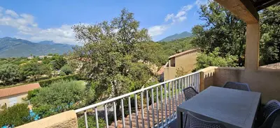 a balcony with a table and chairs and mountains at T2 Résidence Dolce & Vita C4 vue mer et piscine in Propriano