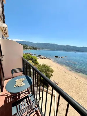a balcony with a table and chairs and a beach at A 20min d AJACCIO, Grand studio 3 personnes - pieds dans l'eau - accès direct plage - vue mer exceptionnelle in Casaglione