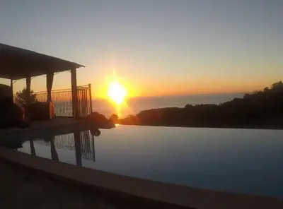 a sunset over a swimming pool with the sun setting at Villa avec vue sur la mer à Sari-Solenzara, piscine privée in Sari Solenzara