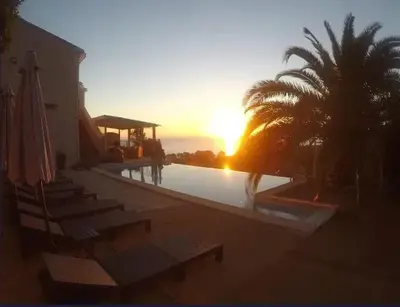 a sunset over a pool with chairs and palm trees at Villa avec vue sur la mer à Sari-Solenzara, piscine privée in Sari Solenzara