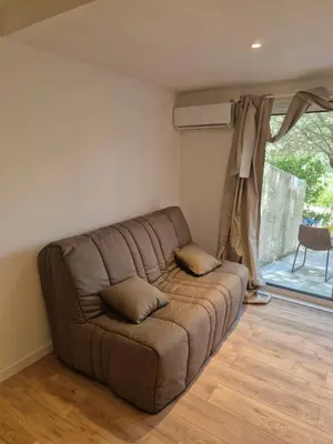 a brown couch in a living room with a window at Studio dans résidence calme in Porto-Vecchio