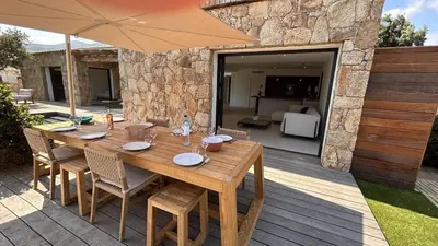 a wooden table with chairs and an umbrella on a patio at Bergerie Piana d'architecte neuve, 8 pers, piscine chauffée, à 10 min plage in Gialla