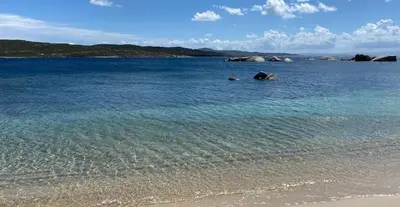 a body of water with a beach and rocks at Villa pieds dans l'eau sur la plage in Pianottoli-Caldarello