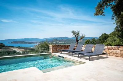 a swimming pool with two chairs next to a stone wall at Villa Toci in Calcatoggio