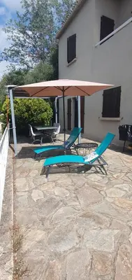 two chairs and an umbrella on a patio at Appt cosy rez de villa in Furiani