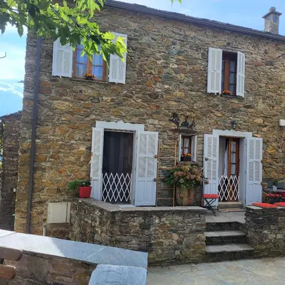 a stone house with white shuttered windows and stairs at Maison de village in Silvareccio