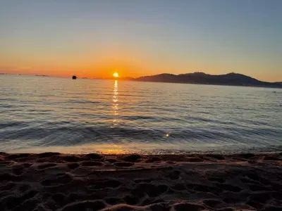 a sunset on a beach with the sun setting over the water at A Nepita - 150m de la plage in Pietrosella