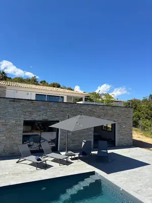 a patio with chairs and an umbrella and a swimming pool at Villa Bavella in Zonza