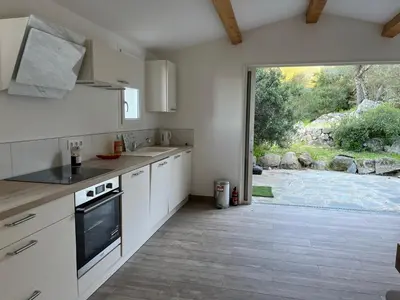 a kitchen with white cabinets and a large sliding glass door at La campagne au bord de la mer in Porto-Vecchio