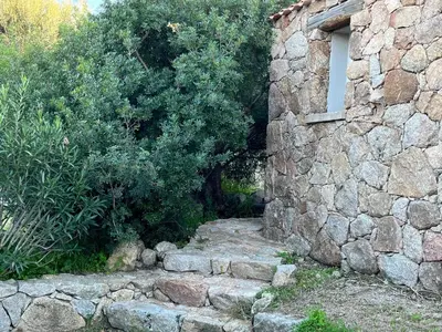 a stone building with a stone path next to a bush at La campagne au bord de la mer in Porto-Vecchio